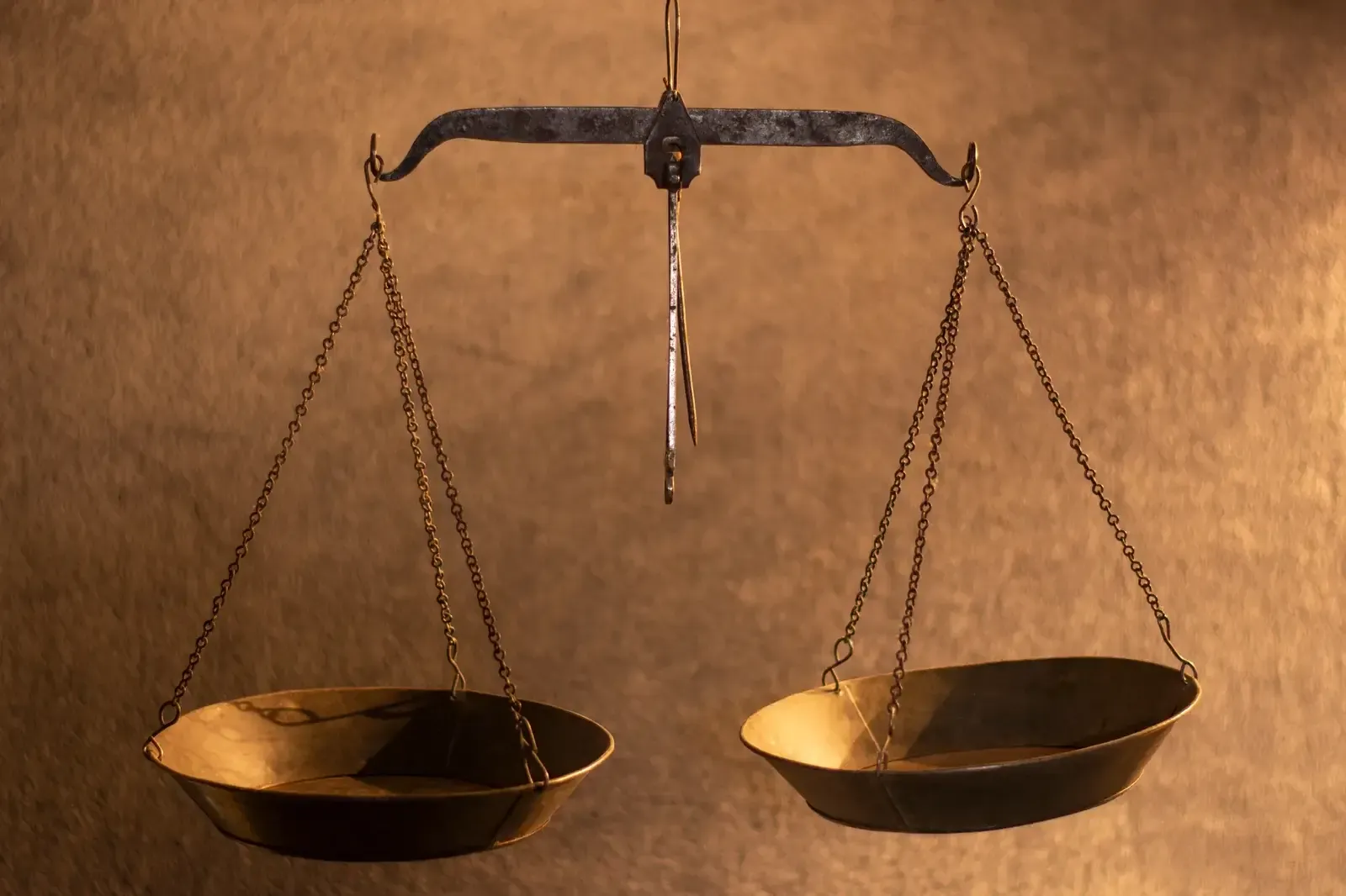 Balance à fléau ancienne suspendue, ses deux plateaux de laiton en équilibre devant un fond ocre lumineux