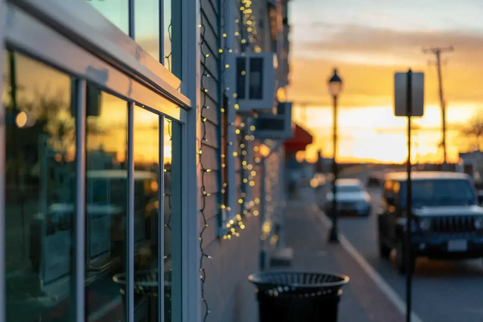 Vitrine de commerce à l’ossature vert d’eau ornée d’une guirlande lumineuse, dans une rue baignée par la lumière orangée du coucher de soleil