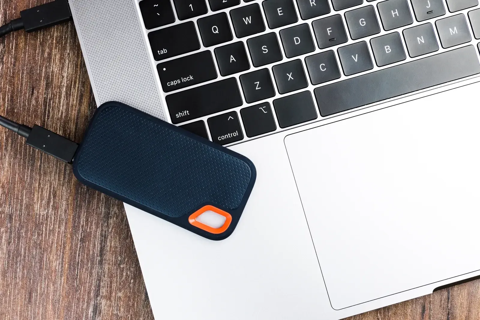 Disque SSD externe noir à détail orange, branché à un ordinateur portable posé sur une planche de bois brut
