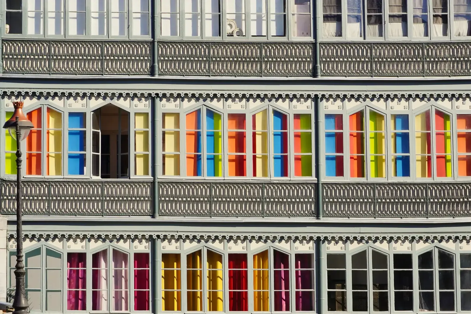 Façade d’un immeuble ancien de Pau, ses volets et panneaux peints en rouge, orange, jaune, vert et bleu alignés sur trois niveaux de fenêtres à balustrades