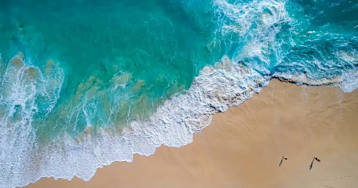 Littoral vu du ciel : l'eau passe du bleu profond au turquoise clair au-dessus d'un banc de sable doré