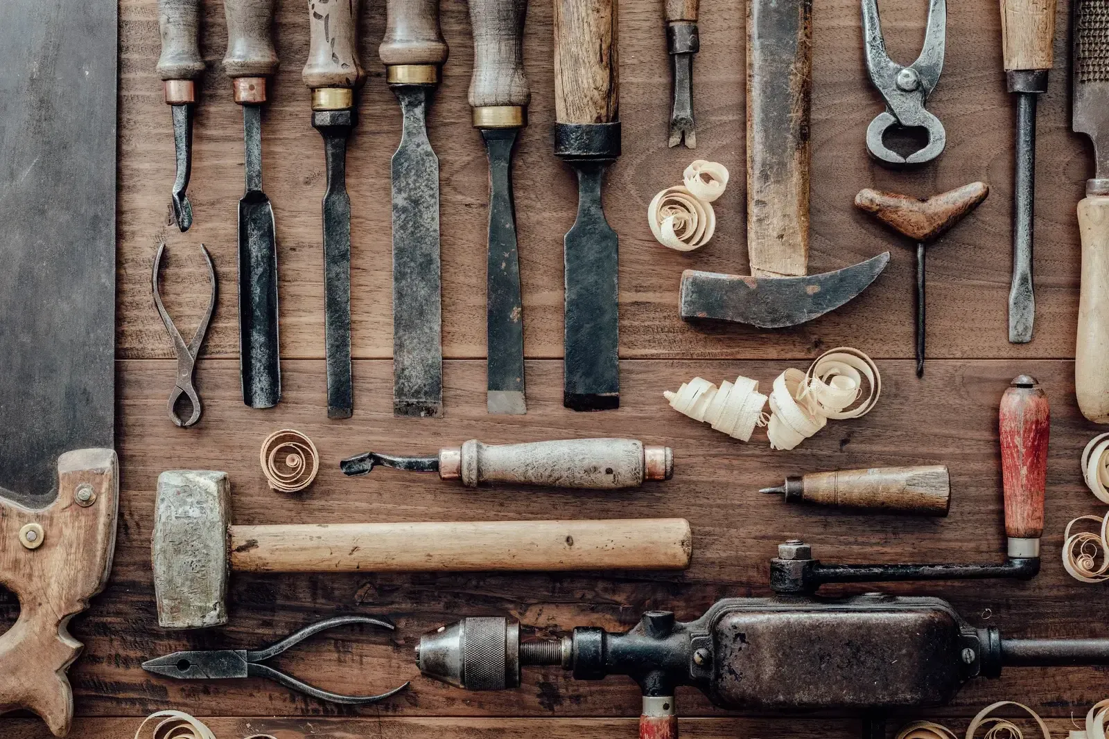 Ciseaux à bois, maillet, vilebrequin et outils anciens alignés sur un établi en bois, vus de dessus