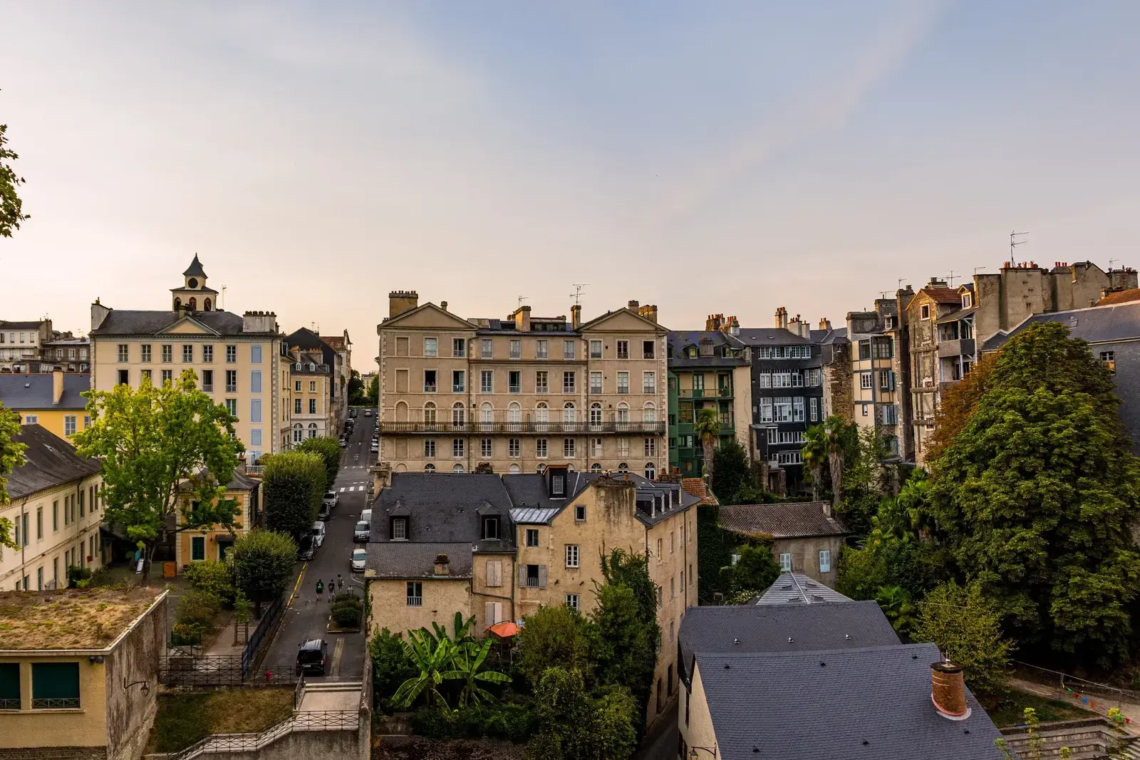 Vue en surplomb des toits et des façades de Pau, clocher sur la gauche et ciel doré de fin de journée