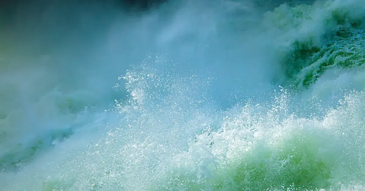 Gros plan d'une vague turquoise translucide traversée par la lumière, crête ourlée d'écume