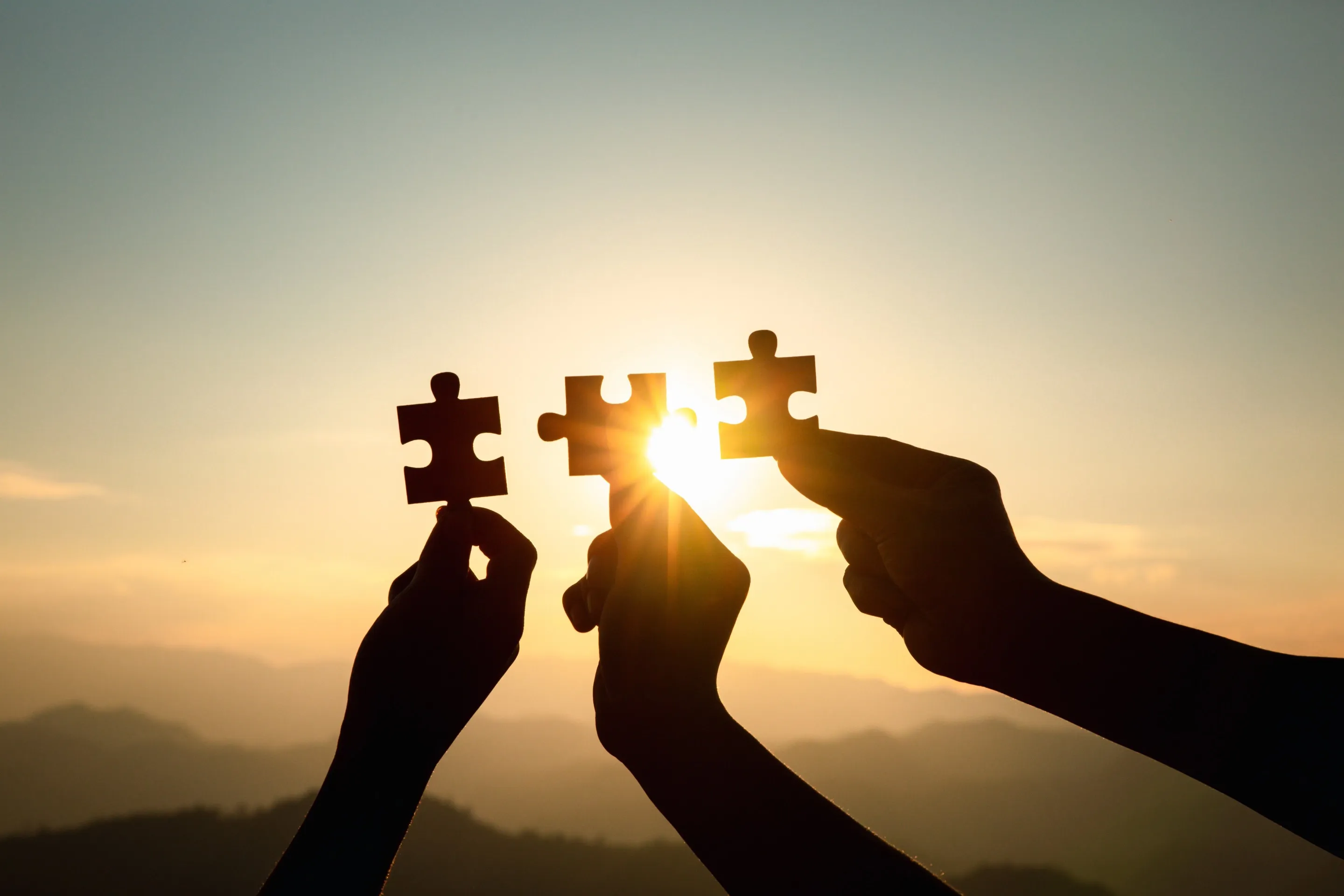 Deux mains rapprochant deux pièces de puzzle à contre-jour, au soleil couchant