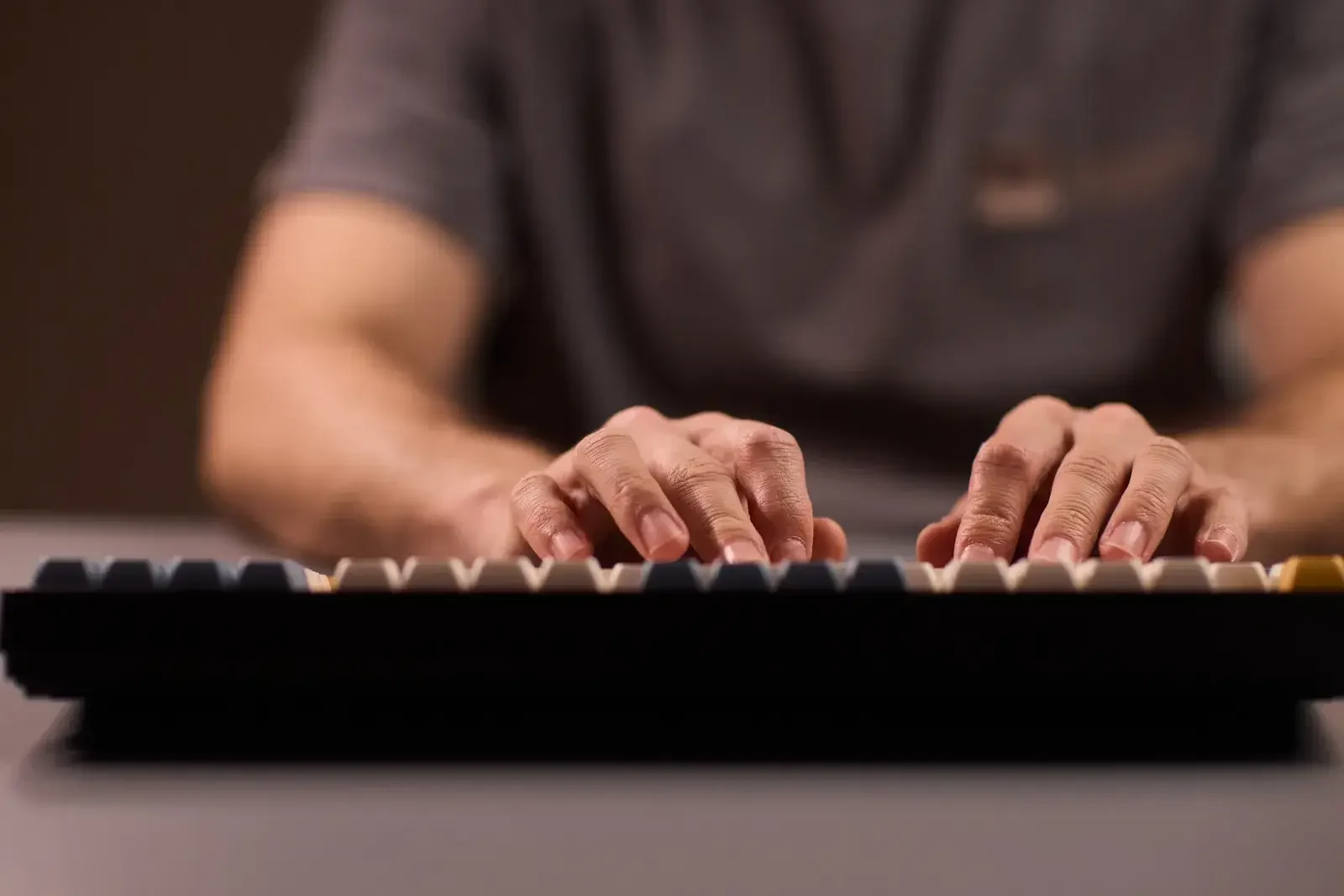 Two hands resting on a black mechanical keyboard, typing, in warm, subdued light