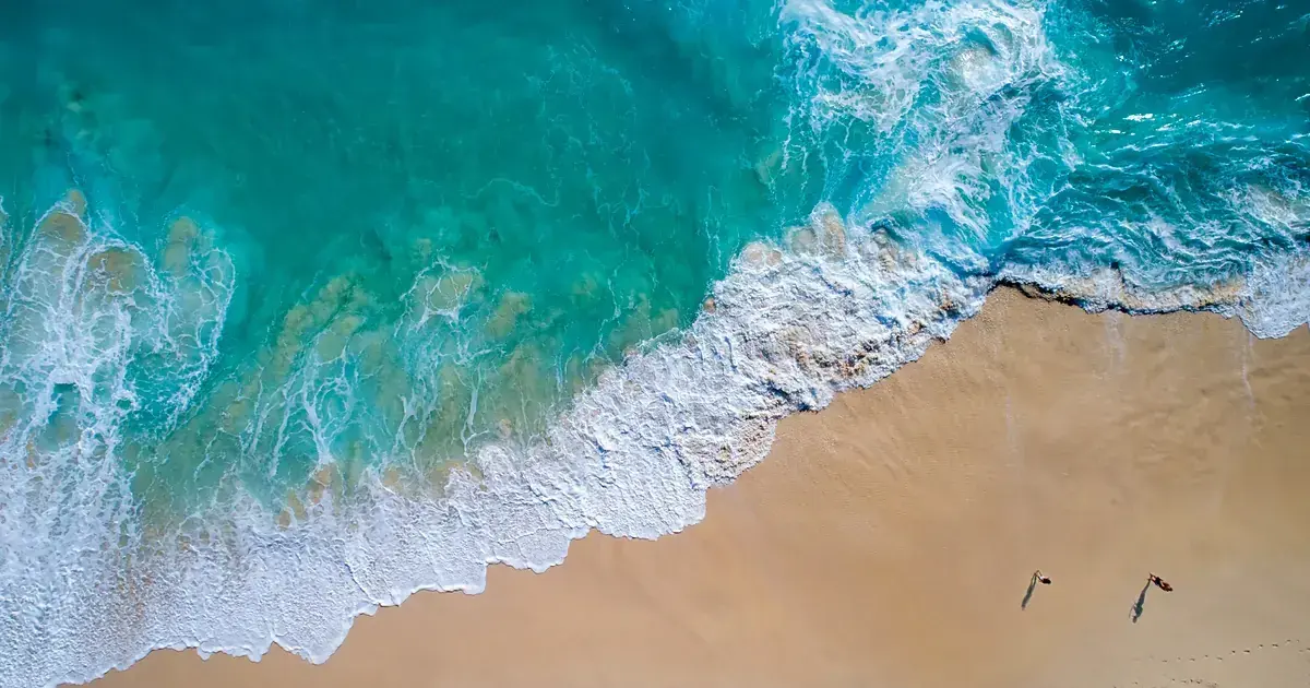 Coastline seen from the air: the water shifts from deep blue to pale turquoise above a golden sandbank