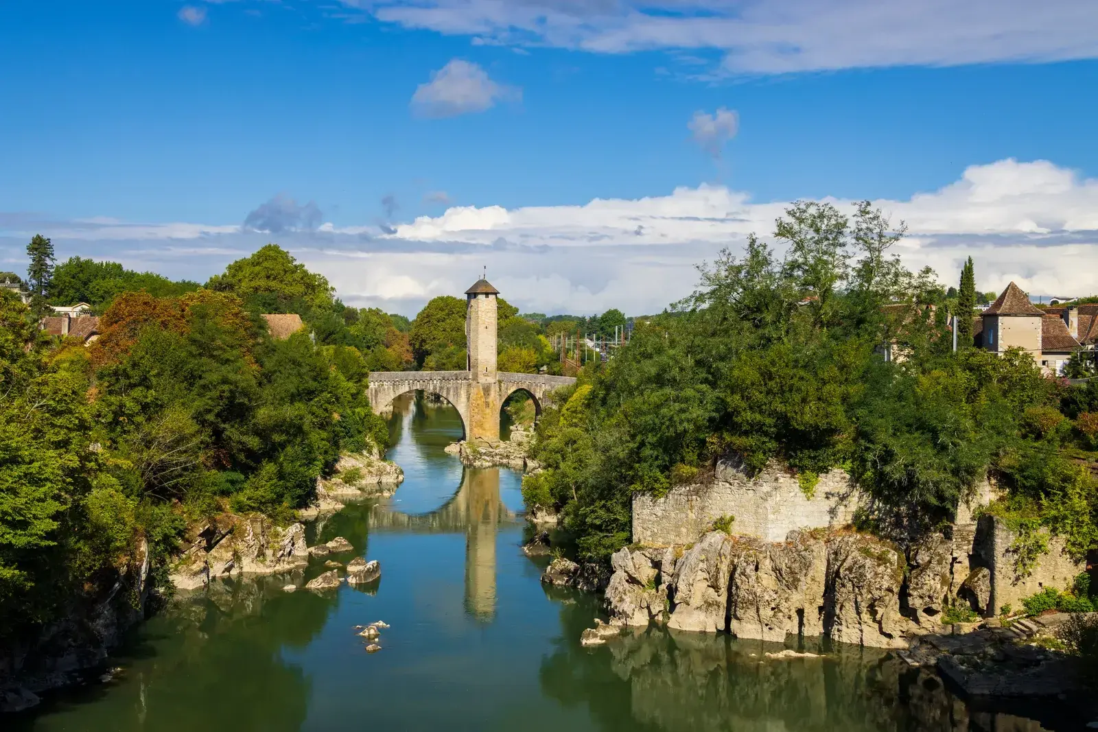 The old fortified bridge at Orthez and its tower crossing the green mountain river between two wooded banks