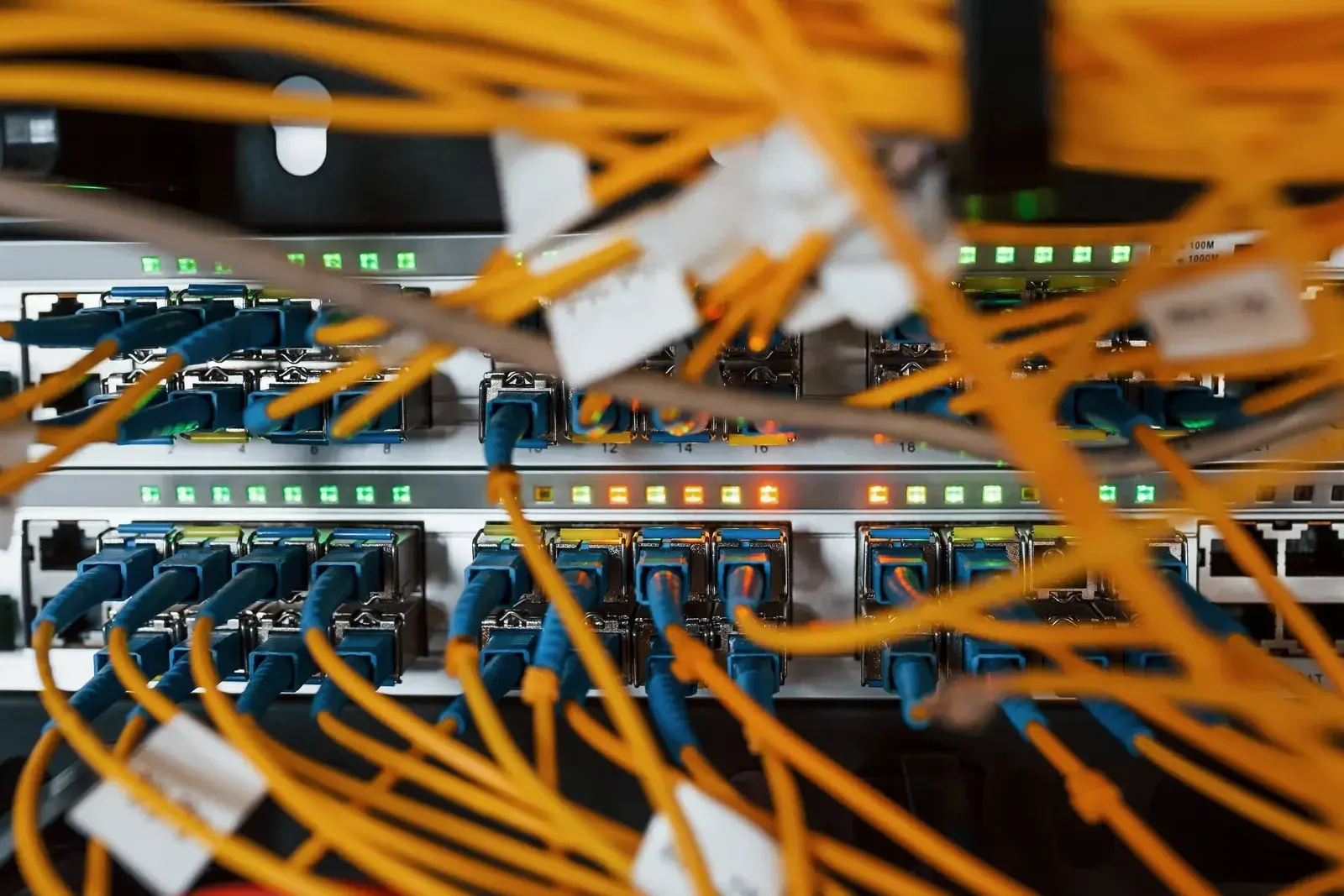 Orange fiber optic cables and blue connectors plugged into the ports of a network switch with green LEDs
