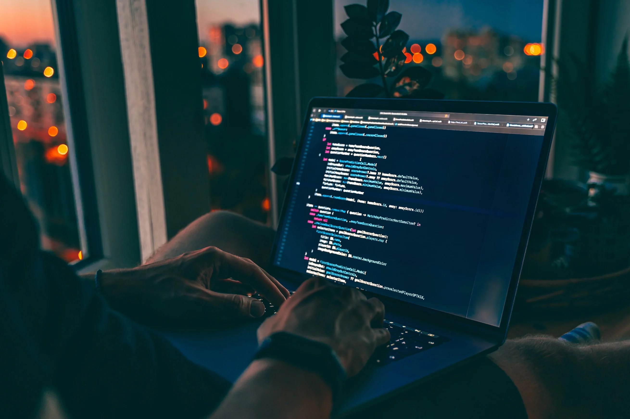 A person working in the evening on a laptop showing lines of code
