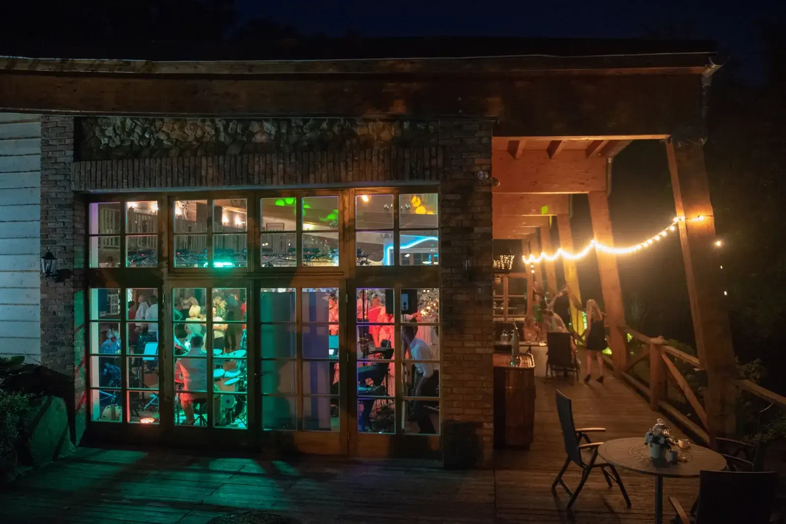 Glass shopfront lit up at dusk, with a string of fairy lights and a wooden terrace