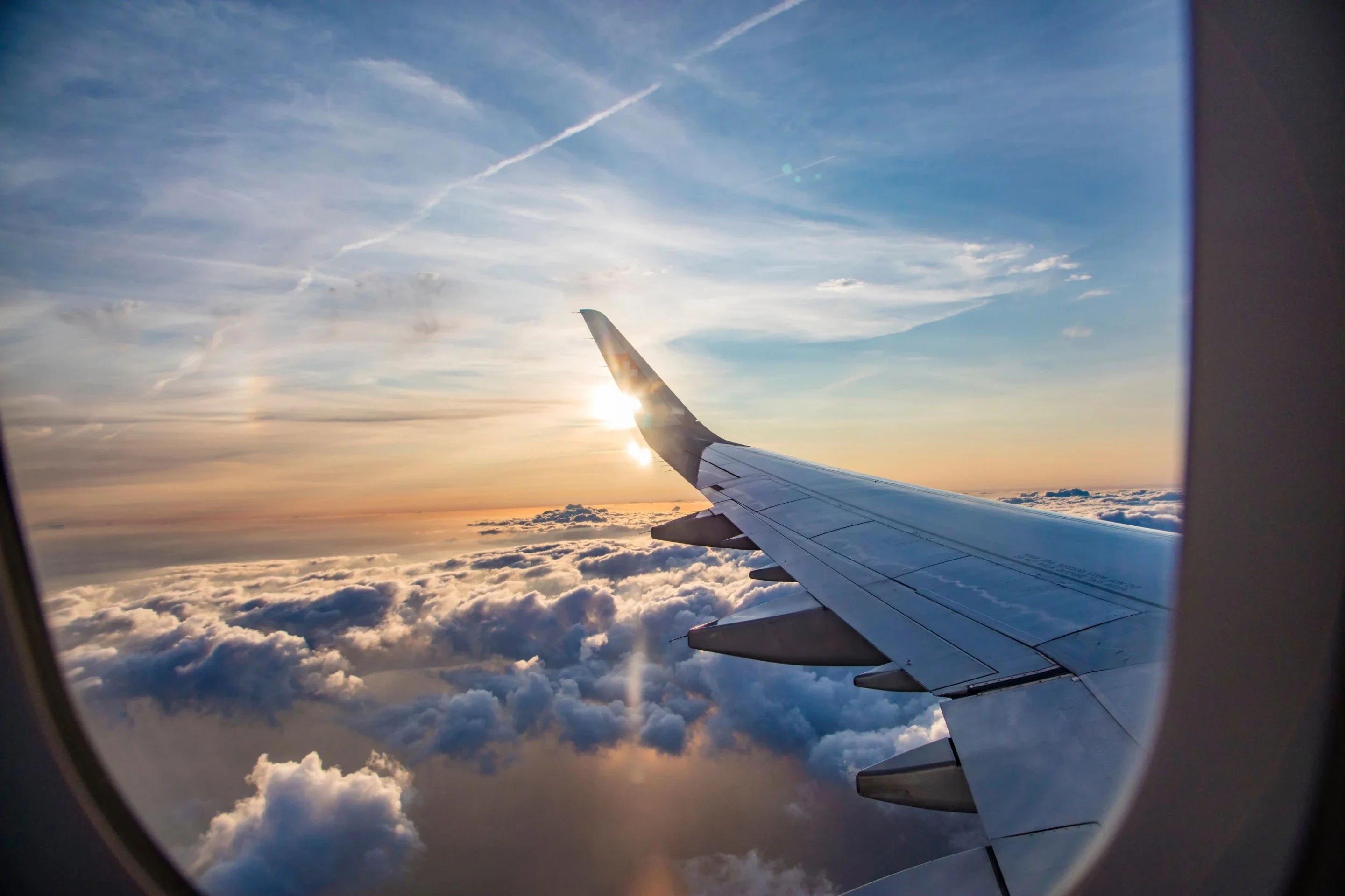 Aircraft wing over a sea of clouds, seen through a cabin window at sunset