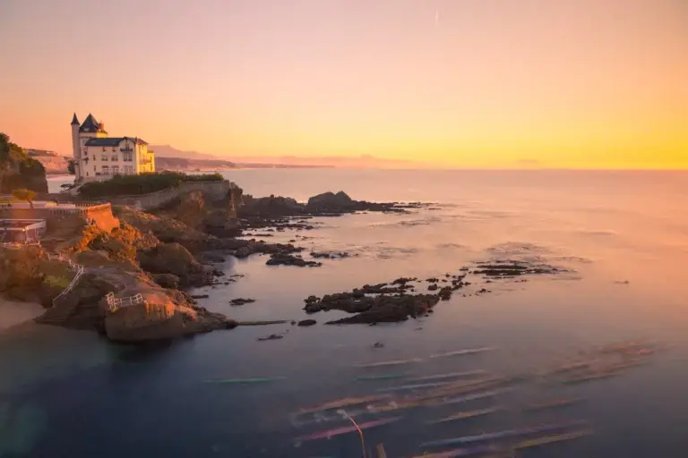 Rochers et villa de bord de mer sur la côte de Biarritz, ciel et océan dorés au coucher du soleil