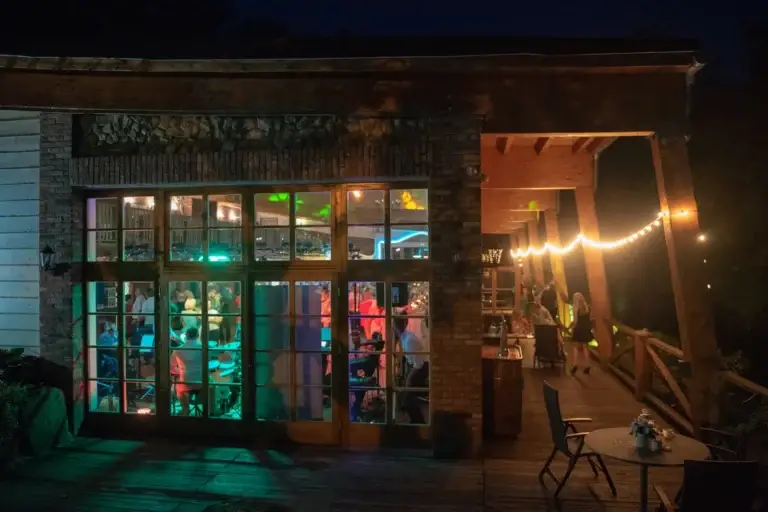 Devanture vitrée d’un commerce éclairée à la tombée de la nuit, guirlande lumineuse et terrasse en bois