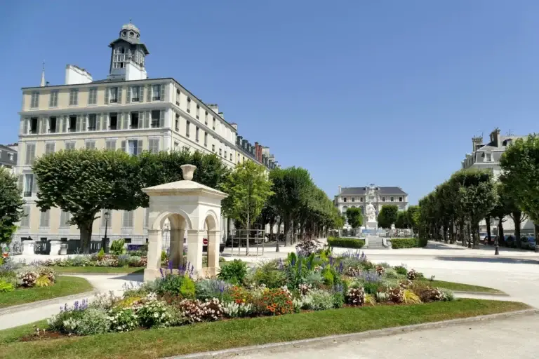 Les parterres fleuris et le kiosque de pierre de la place Royale à Pau, devant la façade claire d’un grand bâtiment public